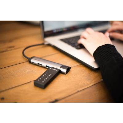 Eine Person tippt auf einem Laptop. Ein USB-Hub mit mehreren Anschlüssen ist angeschlossen und liegt auf einem Holztisch.