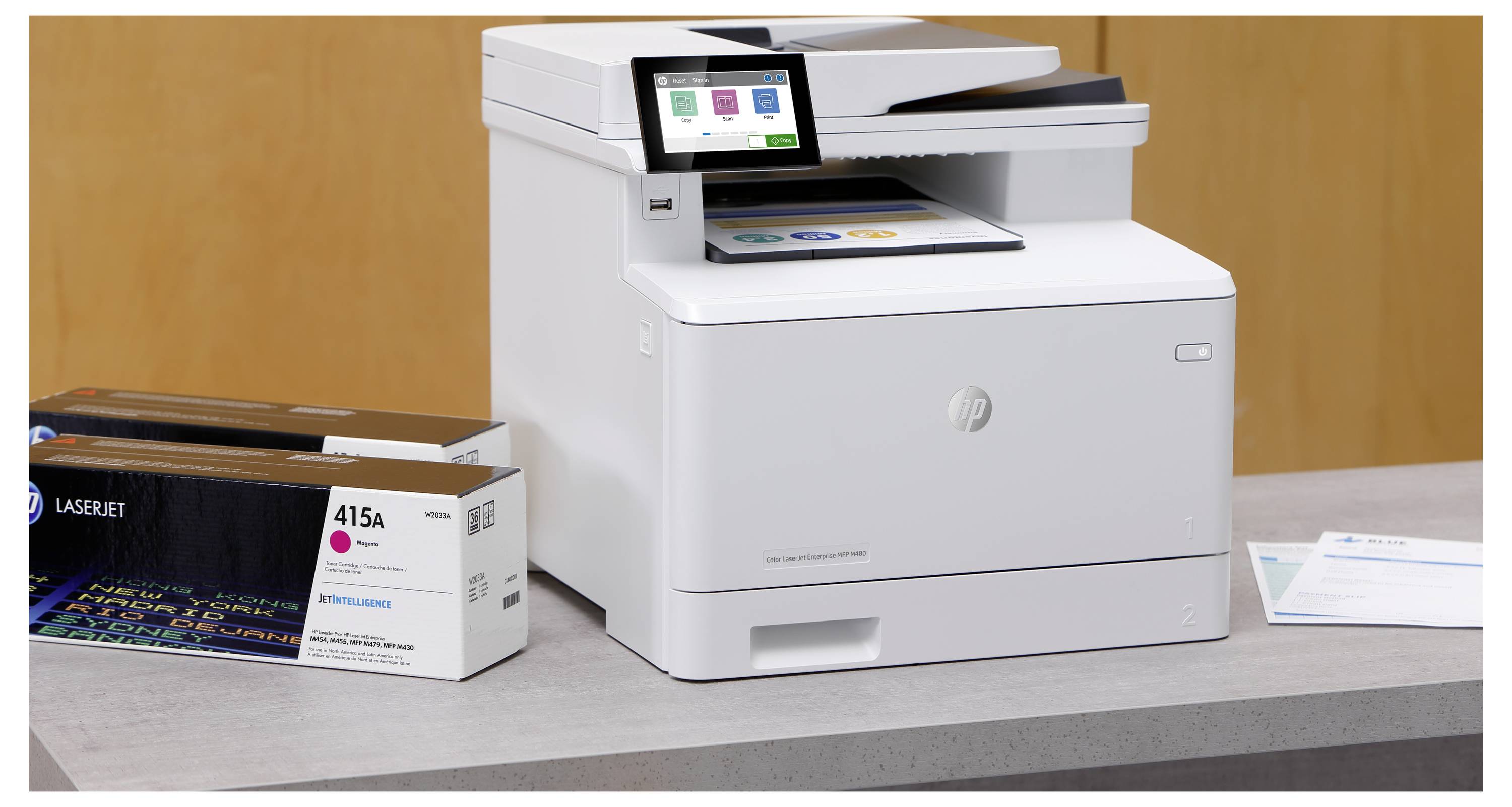 Weißer HP-Multifunktionslaserdrucker auf einem Tisch neben einer Schachtel mit 415A-Tonerpatronen.