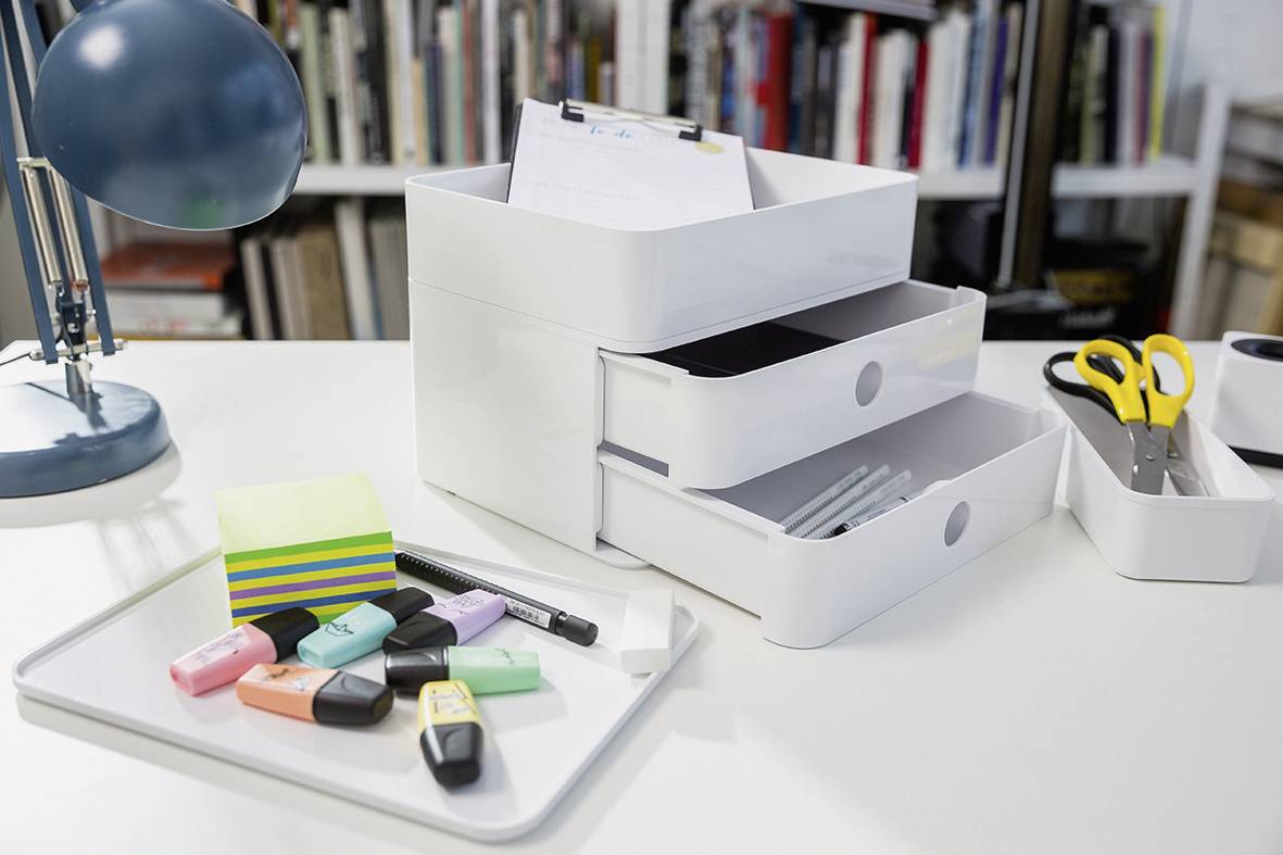 Organisierte Schreibtischutensilien mit Notizblöcken, Textmarkern, Stiften und Schere neben einem Tischleuchtturm.