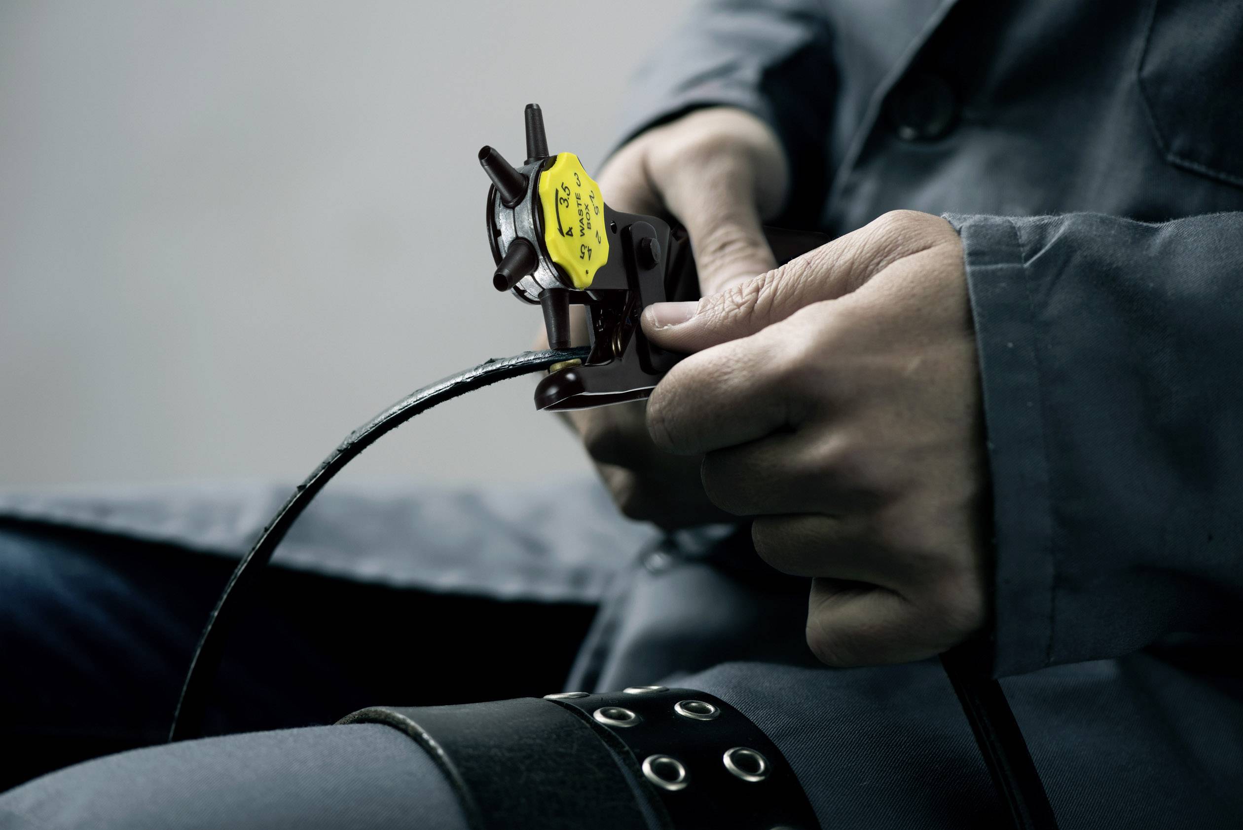 Eine Person in Arbeitskleidung hält ein Werkzeug in der Hand, mit dem sie ein Kabel schneidet oder bearbeitet.