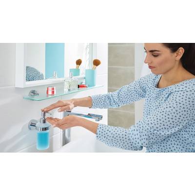 Eine Frau wäscht sich die Hände am Waschbecken. Neben ihr stehen Pflegeprodukte und ein Spiegel hängt darüber an der Wand.