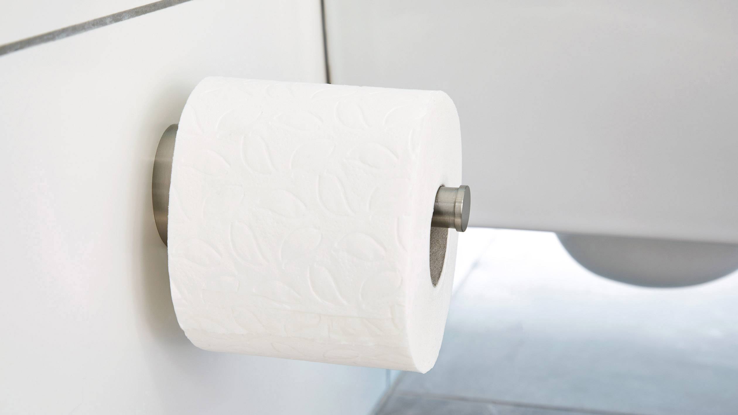 Toilettenpapierrolle, dekorativ mit Blattmuster, an einer Wandhalterung befestigt in einem hellen Badezimmer.
