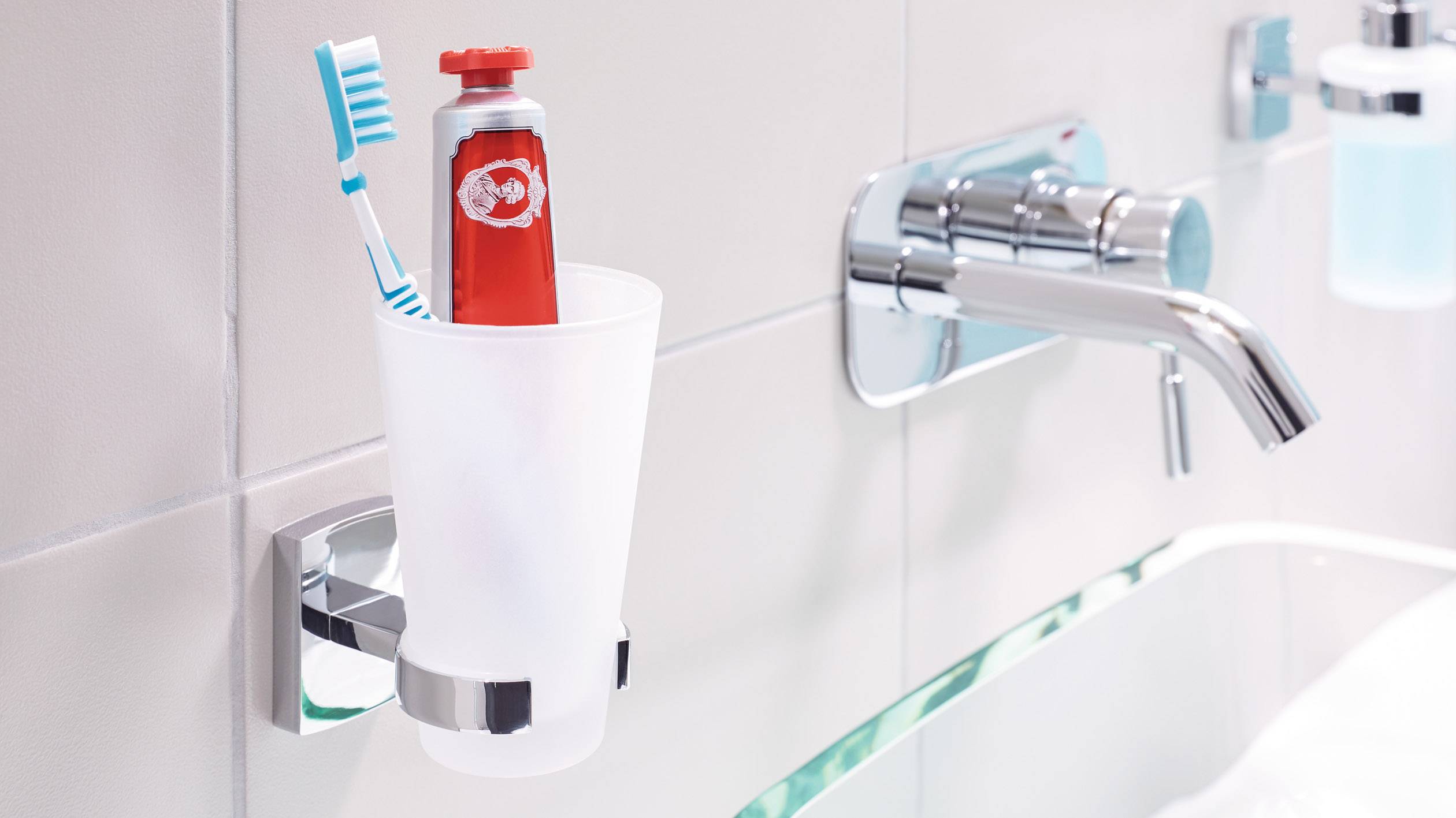 Zahnbürste und Zahnpastatube in einem Becher an der Wand neben einem Wasserhahn im Badezimmer.