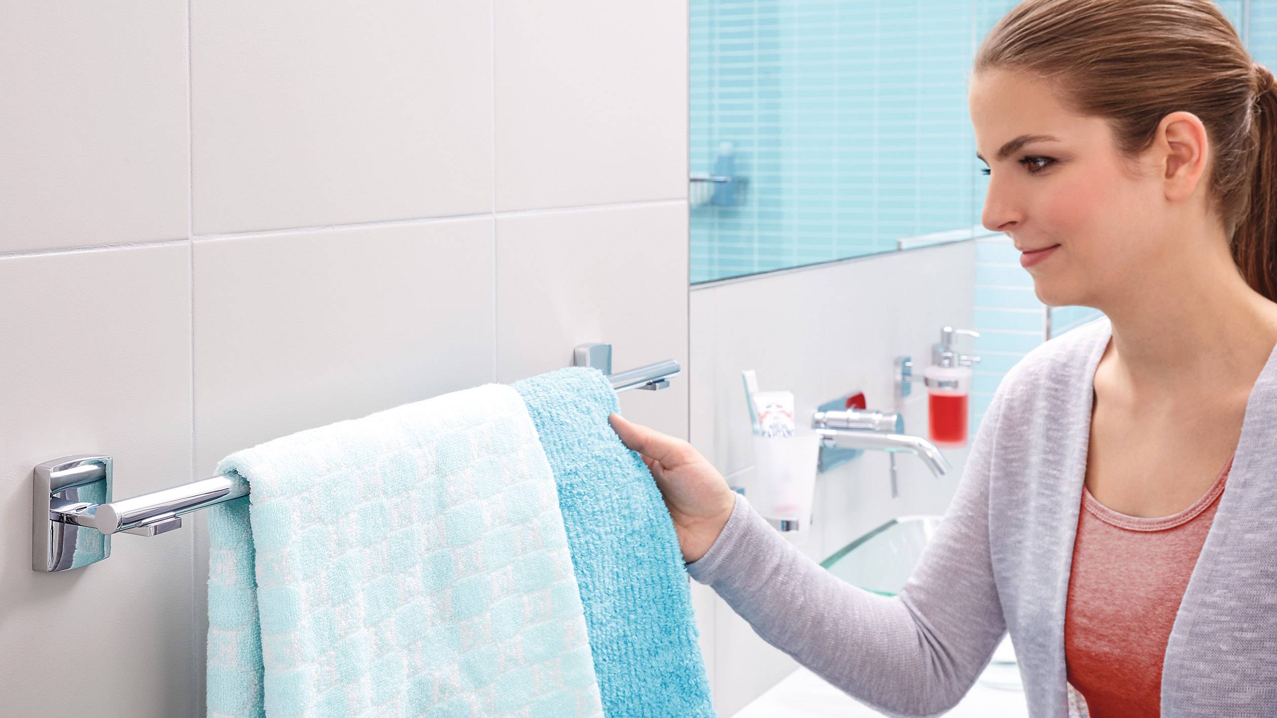 Eine Person hängt ein hellblaues Handtuch in einem modernen Badezimmer mit blauen Fliesen an einen Handtuchhalter.