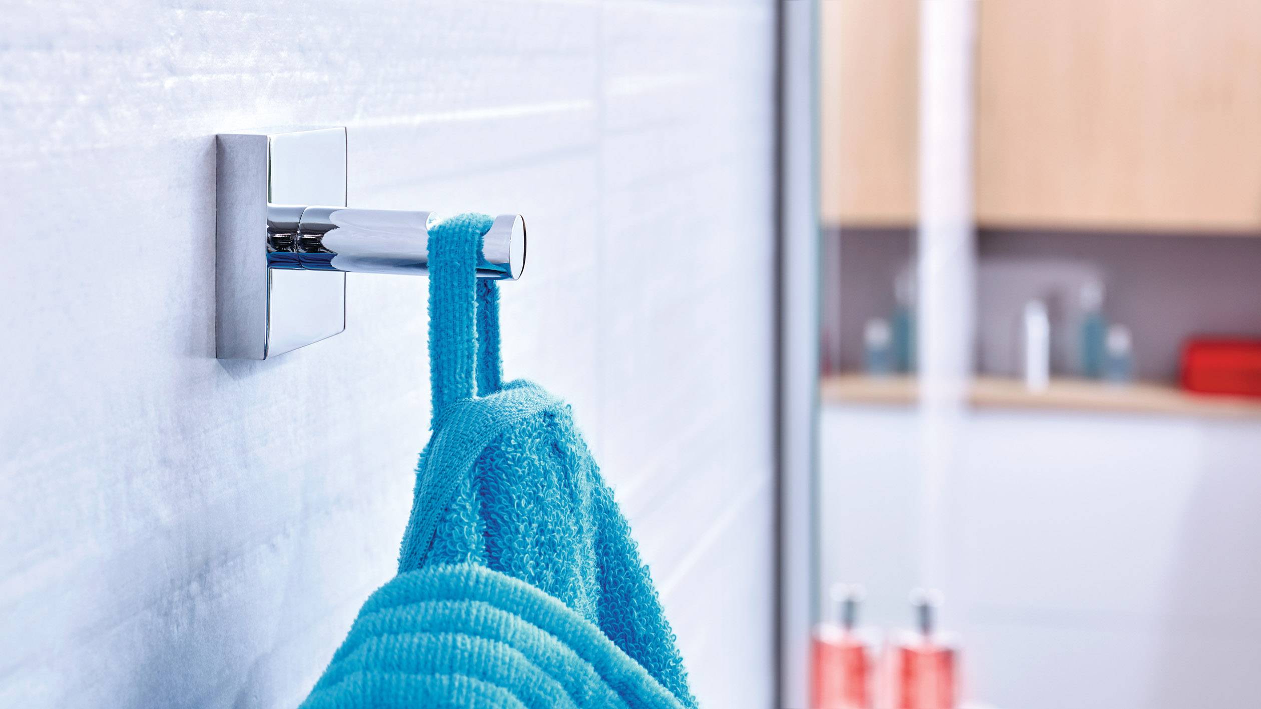 Ein blaues Handtuch hängt an einem silbernen Haken im Badezimmer. Im Hintergrund ist ein unscharfes Regal mit Flaschen sichtbar.