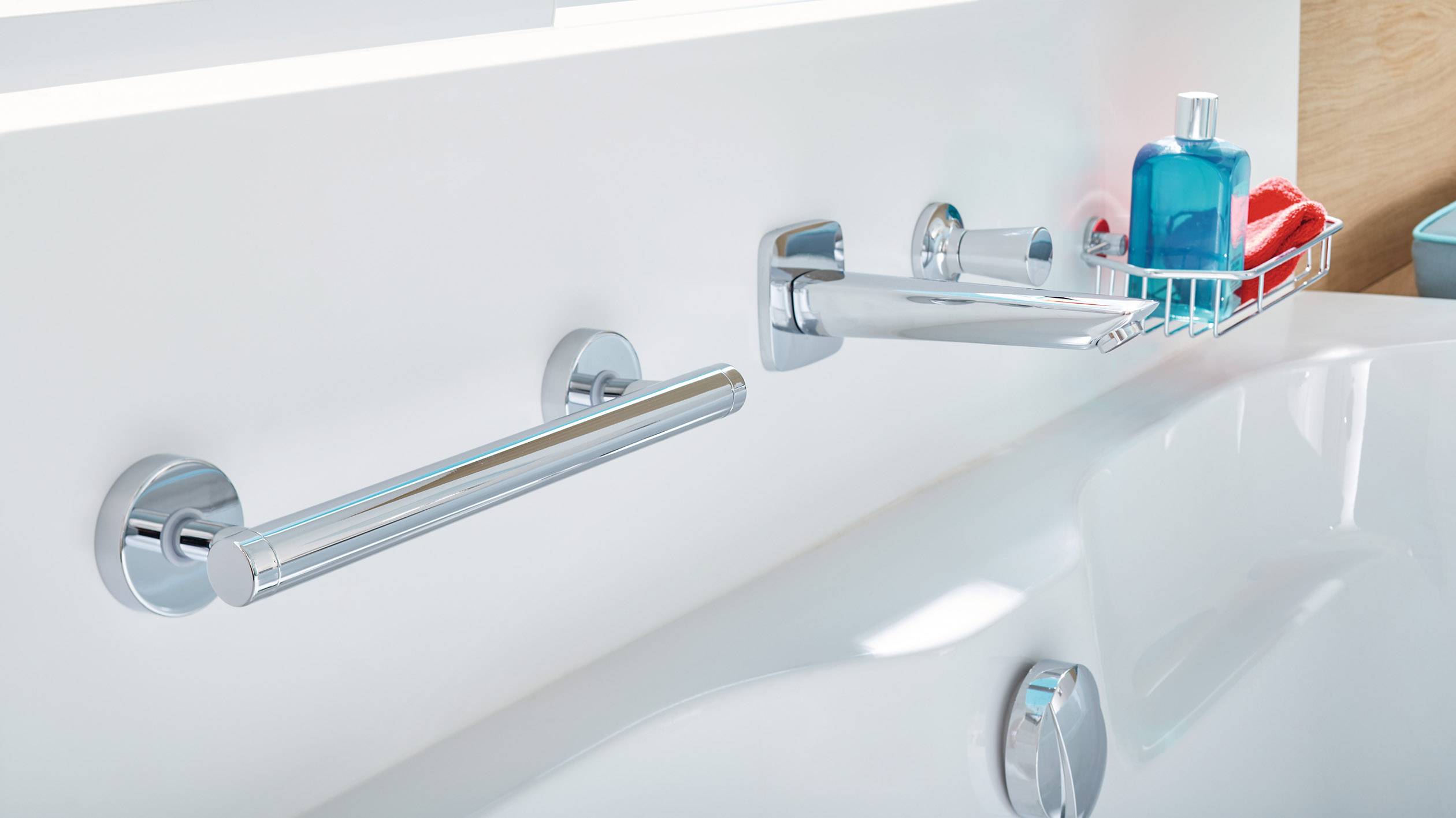 Badezimmerwand mit Haltegriffen, einem Wasserhahn und einer Ablage mit Duschgel und Schwamm über einer Badewanne.