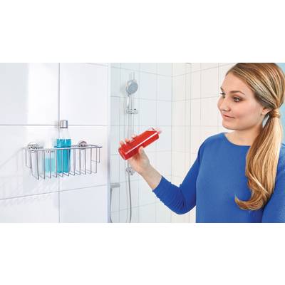 Eine Frau mit langem Haar schaut auf eine rote Flasche in ihrer Hand. Im Hintergrund befindet sich eine Dusche mit Shampoo-Flaschen.