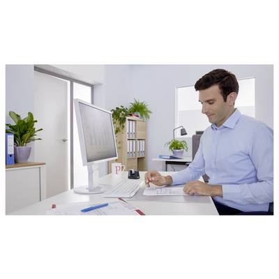 Eine Person in einem blauen Hemd sitzt an einem Schreibtisch in einem hellen Büro und überprüft Dokumente. Ein Computermonitor und Büropflanzen sind im Hintergrund zu sehen.
