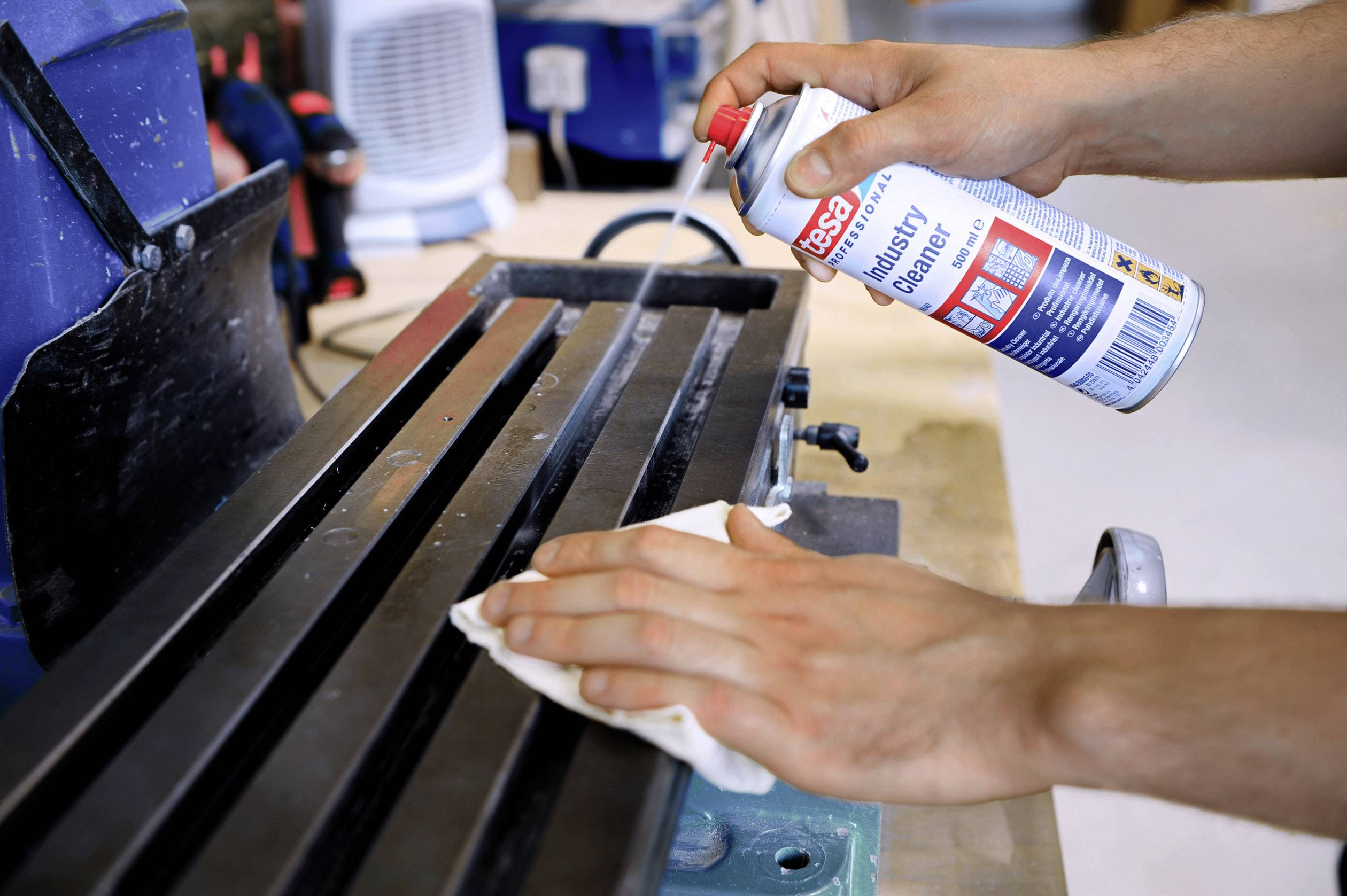 Eine Person reinigt eine Metalloberfläche mit einem Industriereiniger und Tuch.
