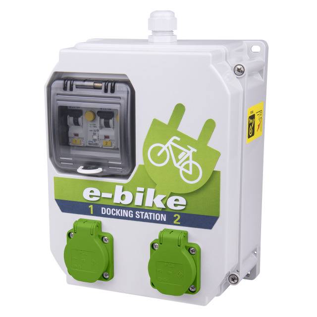 'Weiße E-Bike-Dockingstation mit grünem Fahrradsymbol und zwei Steckdosen. Aufschrift: e-bike 1 Docking Station 2.'