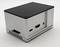 Kleiner, rechteckiger metallener Kasten mit schwarzer Oberseite, mehreren Anschlüssen und Lüftungsschlitzen an der Seite, auf grauem Hintergrund.