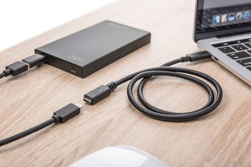 Externe Festplatte verbunden mit einem Laptop auf einem Holztisch; USB-Kabel und Adapter sind sichtbar.