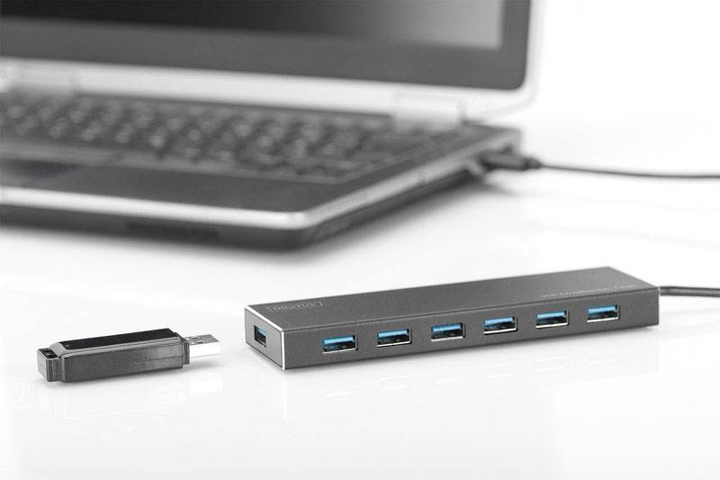 Ein USB-Hub mit sieben Anschlüssen ist neben einem Laptop platziert. Ein USB-Stick liegt daneben auf einem weißen Tisch.