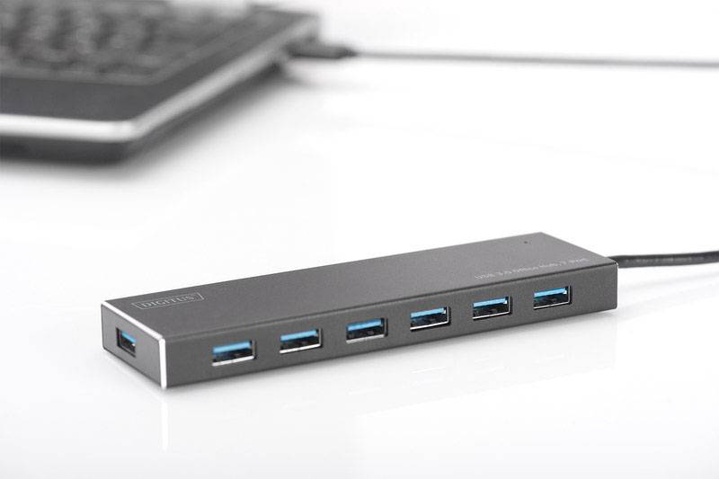 USB-Hub mit sieben blauen Anschlüssen auf einem Schreibtisch, verbunden mit einem Laptop im Hintergrund. Ideal zur Erweiterung von USB-Anschlüssen.