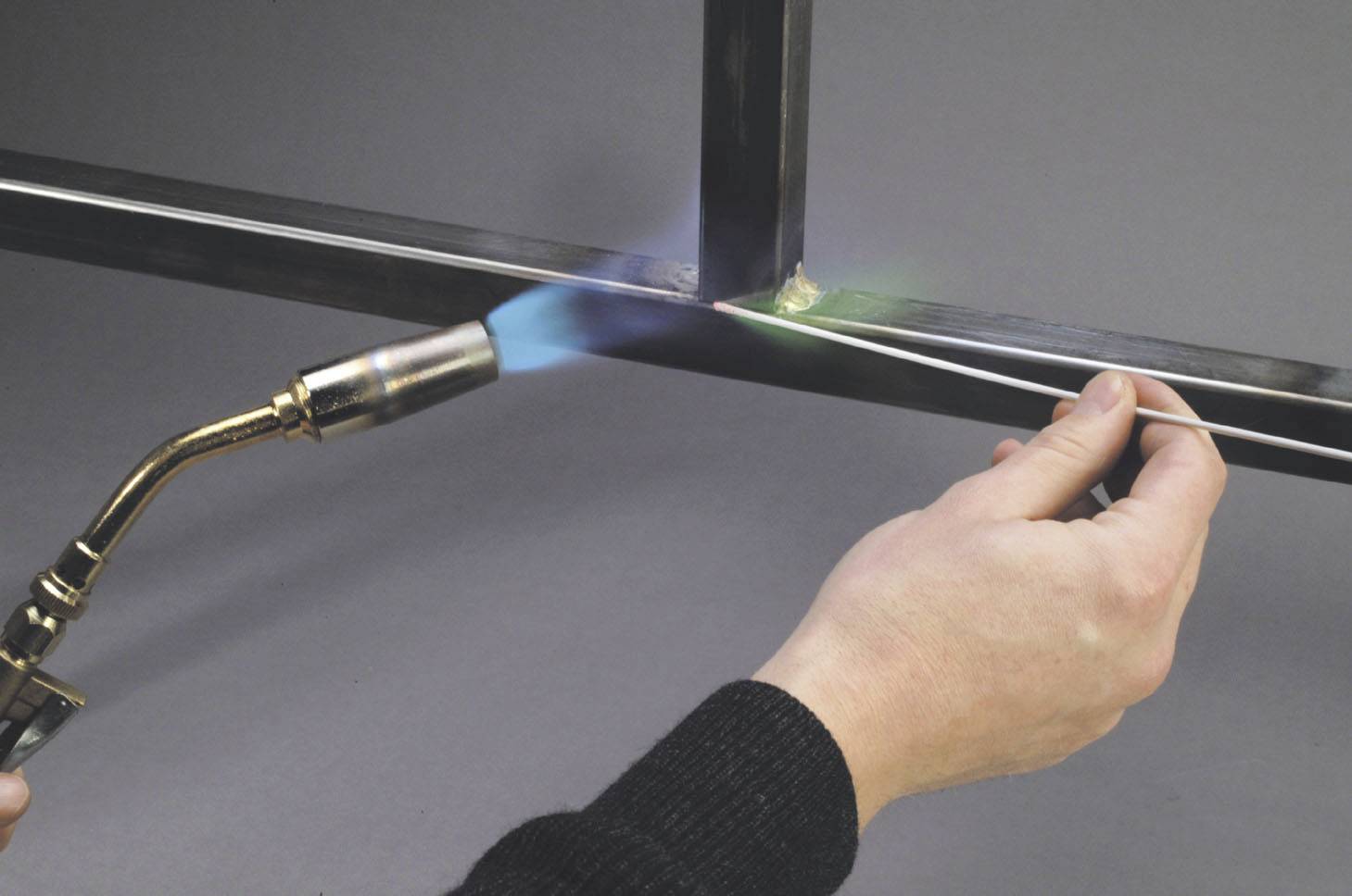 Eine Person lötet Metallrahmen mit einem Handbrenner. Die Flamme erhitzt die Verbindungsstelle, während Lötmaterial hinzugefügt wird.