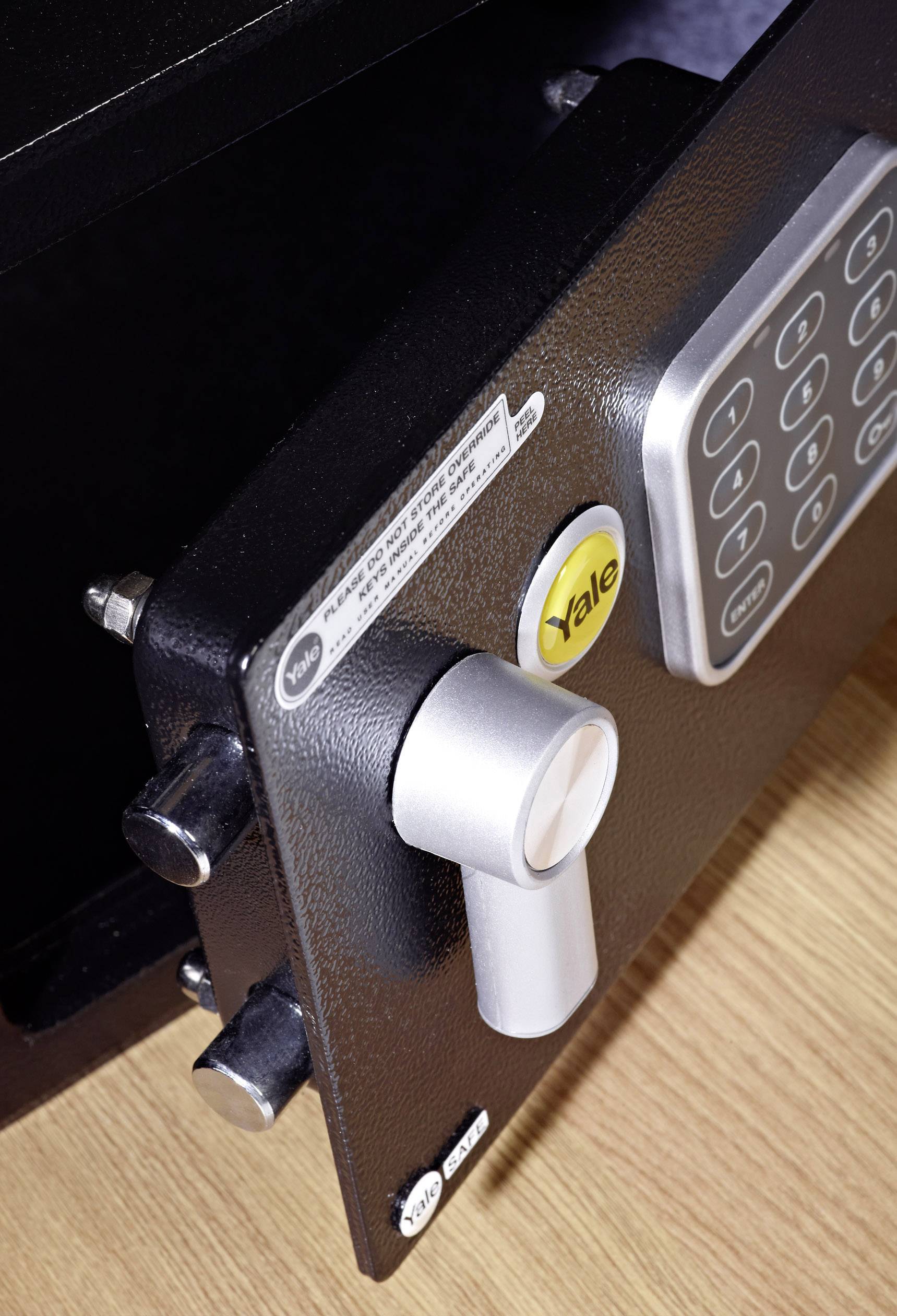 Geöffneter Safe mit elektronischem Tastenfeld und Drehgriff sichtbar. Der Safe steht auf einer Holzoberfläche.