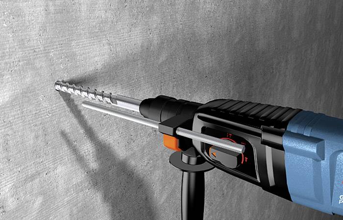 Bohrmaschine mit eingesetztem Bohrer bohrt ein Loch in eine Betonwand. Der Bohrer hat einen schwarzen Griff und einen blauen Körper.