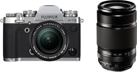Eine Systemkamera von Fujifilm mitsamt aufgeschraubtem Objektiv und ein passendes Wechselobjektiv vor weißem Hintergrund