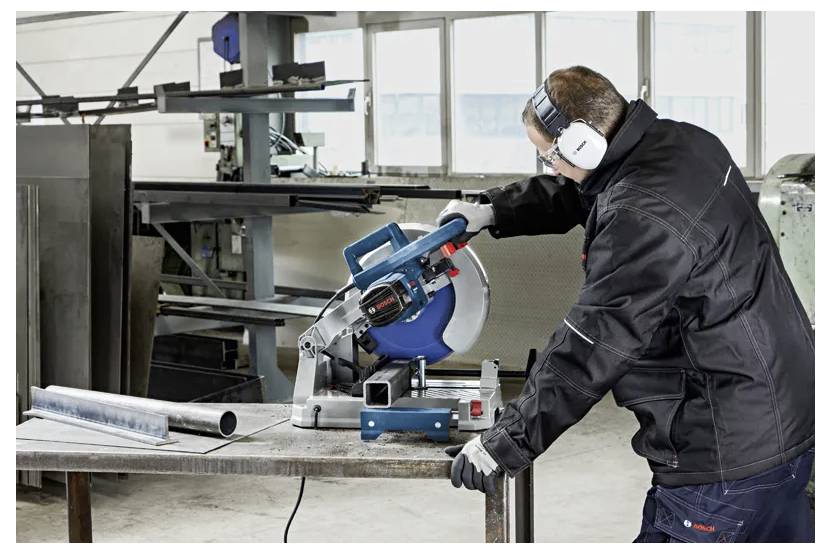 Eine Person in Schutzausrüstung verwendet eine Kreissäge, um Metallrohre in einer Werkstatt zu schneiden, wobei Sicherheit und Präzision in der industriellen Arbeit betont werden.