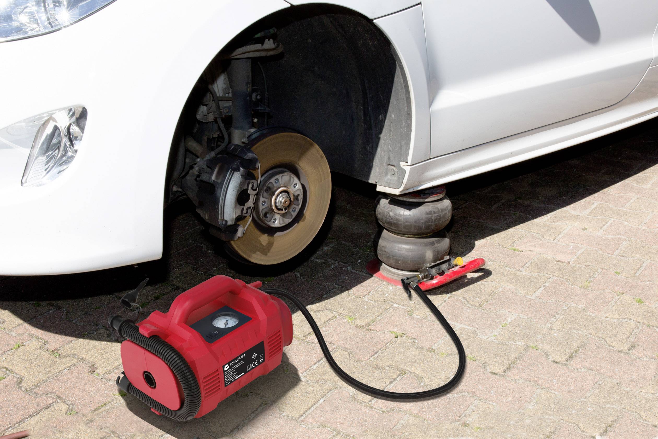 Ein Auto wird mit einem Druckluftheber angehoben, wobei kein Rad an der Vorderachse montiert ist. Ein Kompressor ist neben dem Auto platziert.