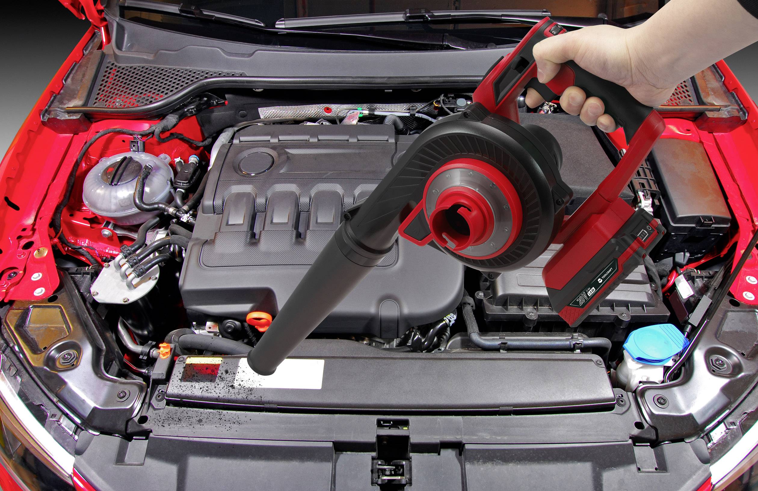 Eine Hand hält einen Staubsauger über einen geöffneten Auto-Motorraum, um Schmutz zu entfernen.