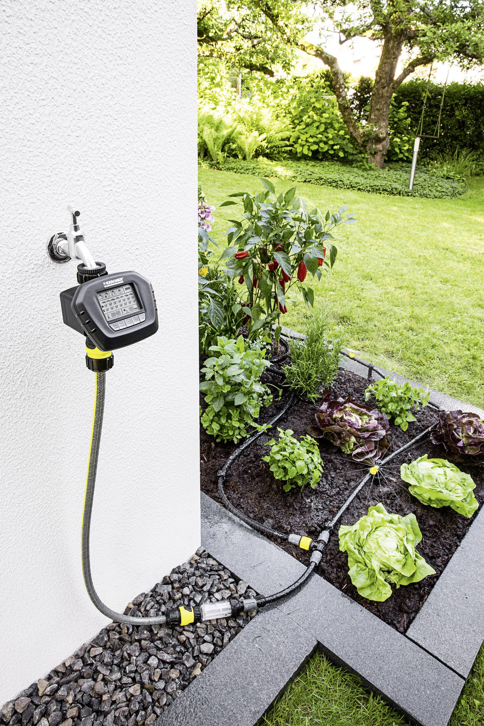 Automatisches Bewässerungssystem im Garten, das Pflanzen wie Salat, Kräuter und Paprika versorgt. Garten mit grünem Rasen im Hintergrund.