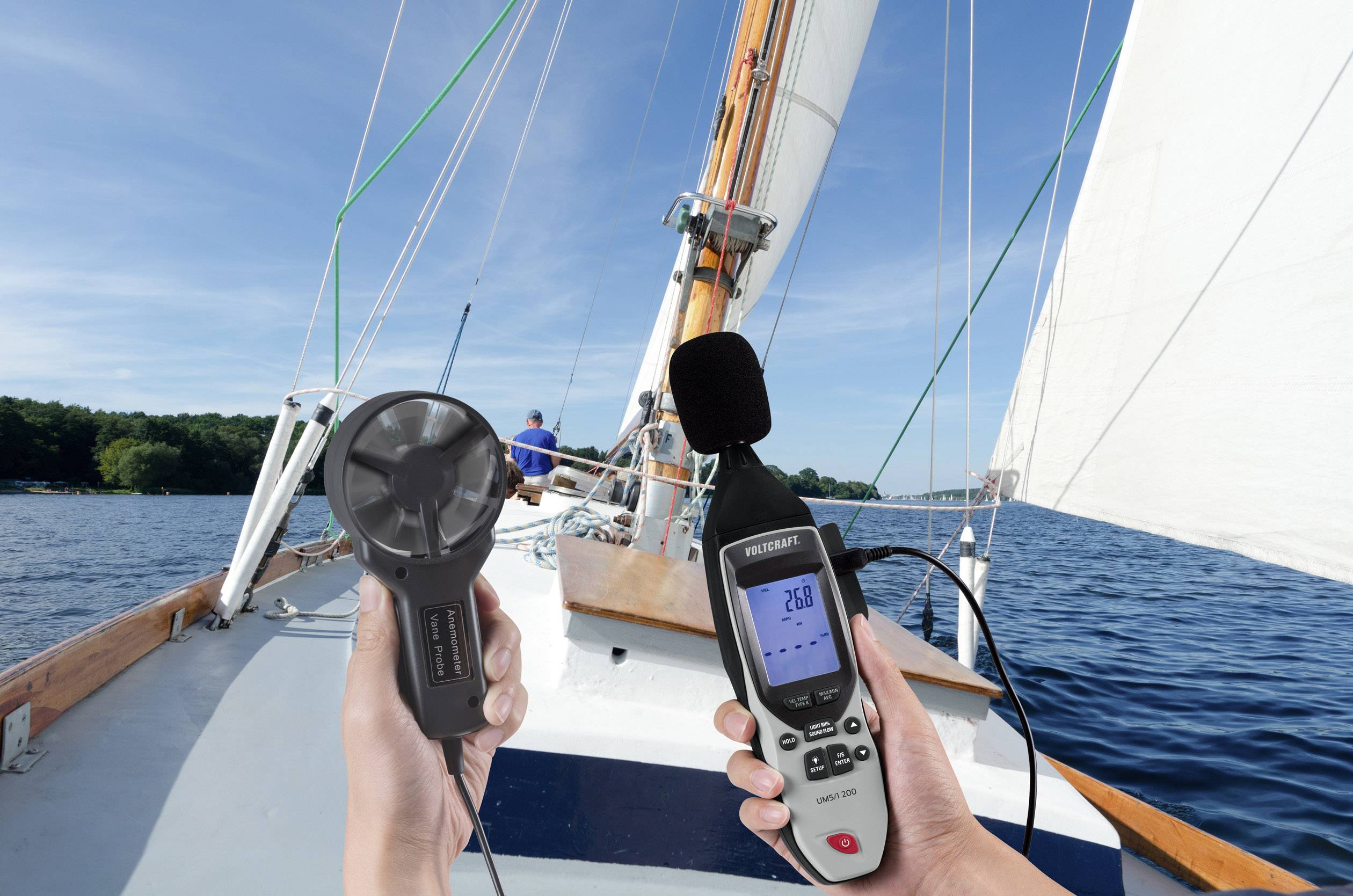 Eine Person auf einem Segelboot misst mit einem Anemometer die Windgeschwindigkeit. Das Boot segelt bei klarem Himmel auf einem See.