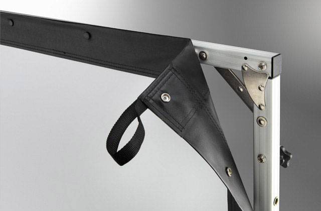 Nahaufnahme einer Ecke eines Projektionstuchs, das an einem Aluminiumrahmen befestigt ist. Ein schwarzes Band hängt lose an der Ecke.