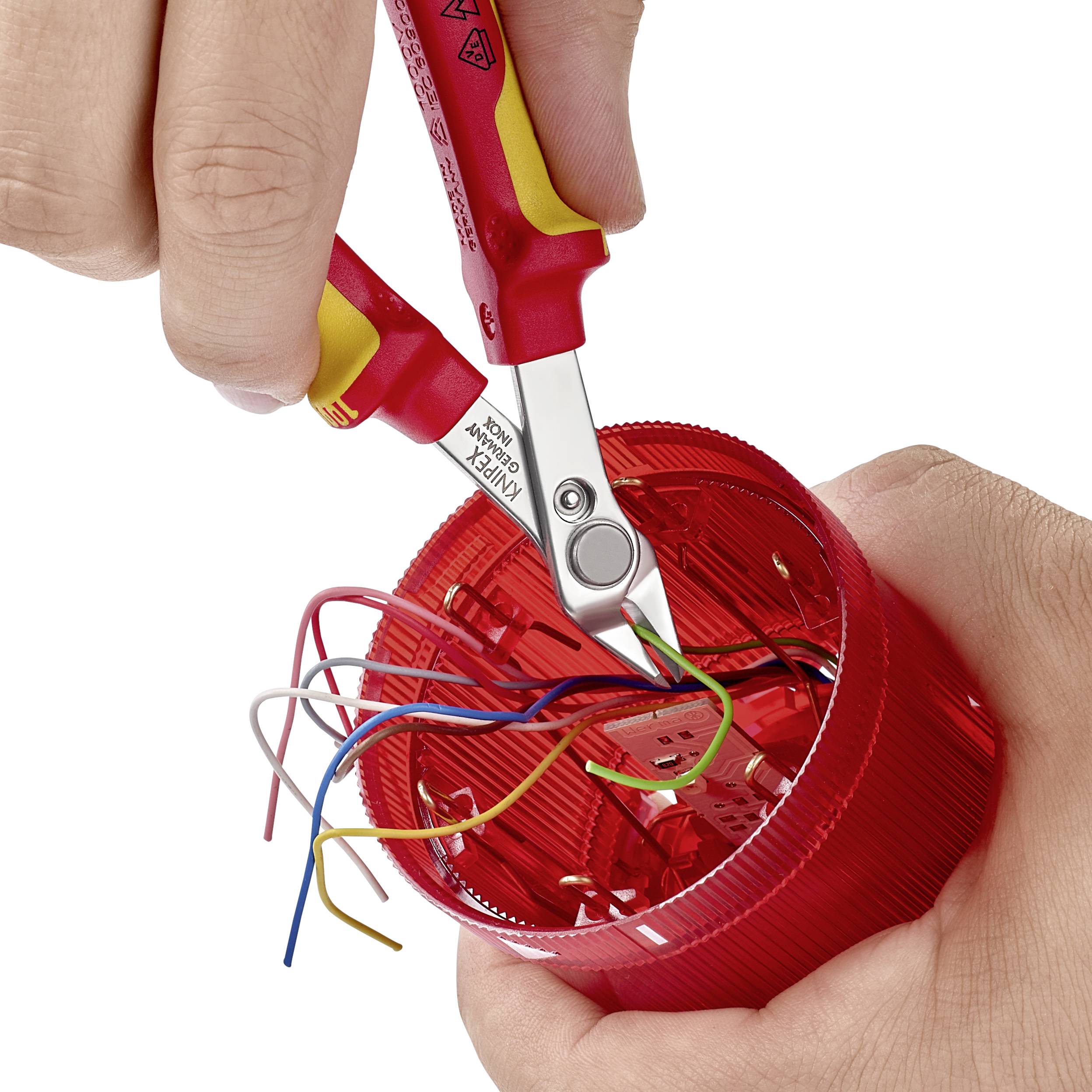 Eine Hand benutzt einen Drahtschneider, um bunte Kabel in einem roten Plastikgehäuse zu schneiden.