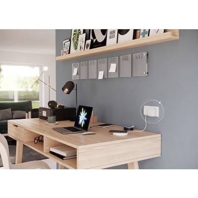 Moderner Arbeitsplatz mit Holzschreibtisch, Laptop, Lampe und Wandregal mit Fotos. Im Hintergrund ein Wohnzimmer mit Sofa.