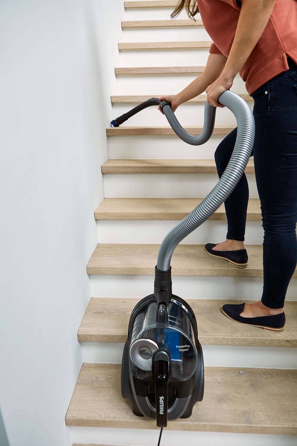 Eine Person saugt mit einem Staubsauger die Treppe ab. Der Staubsauger steht sicher auf einer Treppenstufe.