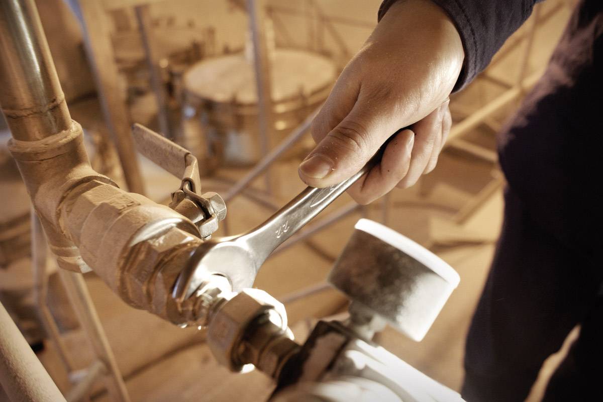 Eine Person zieht in einer industriellen Umgebung mit einem Schraubenschlüssel eine Rohrverbindung fest.