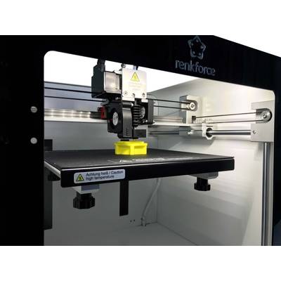 Ein 3D-Drucker druckt ein gelbes Objekt. Warnschild auf der Plattform: 'Achtung heiß / Caution high temperature'.