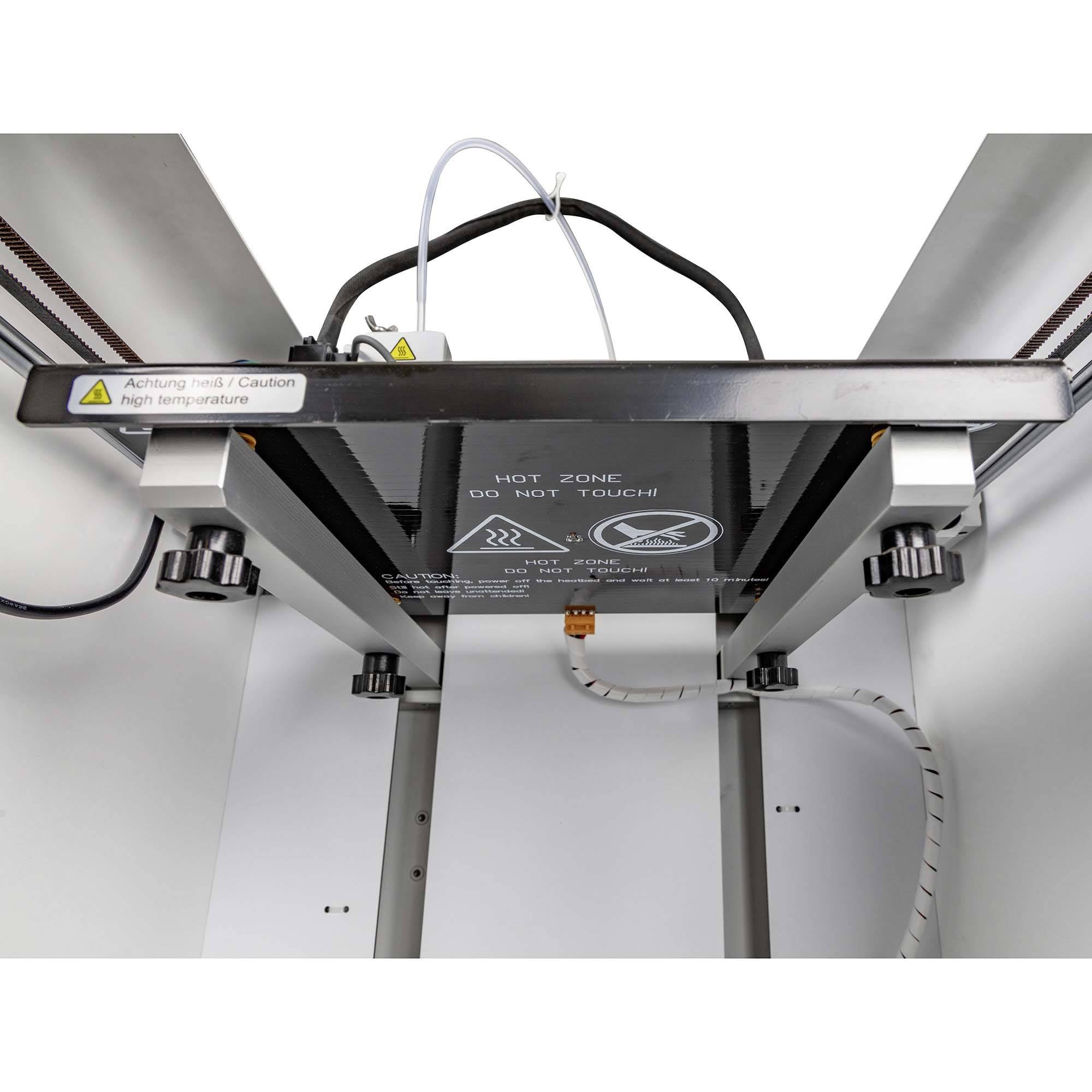 3D-Drucker von unten gesehen mit einem Warnhinweis: 'Hot Zone - Nicht berühren!'. Kabel und mechanische Teile sichtbar.