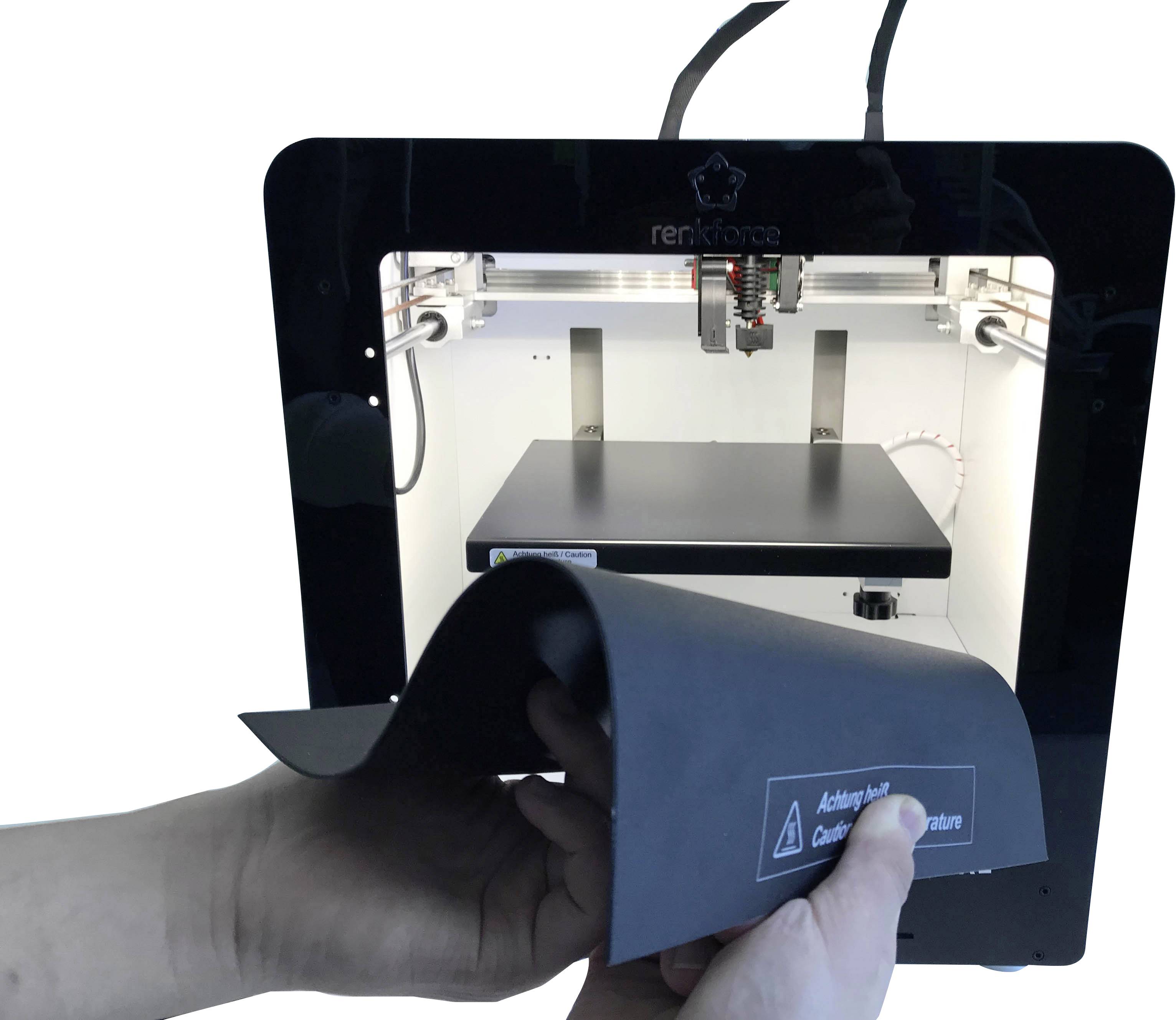 Ein 3D-Drucker druckt ein Objekt aus Kunststoff. Hände halten eine flexible Druckplatte mit einem Sicherheitshinweis.