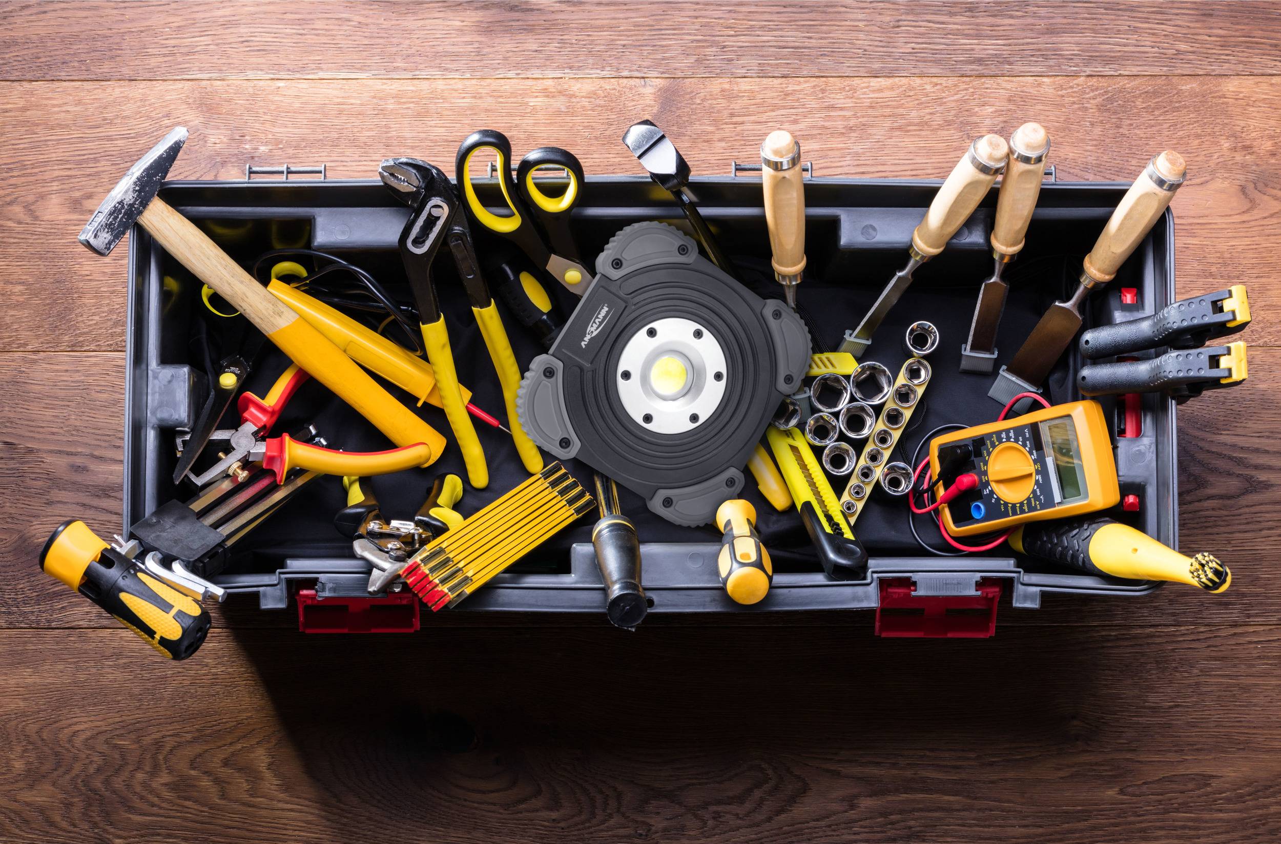 Werkzeugkasten mit verschiedenen Handwerkzeugen wie Hammer, Schraubenzieher, Maßband und Zangen auf einem Holzboden.