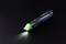 Ein batteriebetriebener Stifthighlighter leuchtet mit grünem Licht auf dunklem Hintergrund.