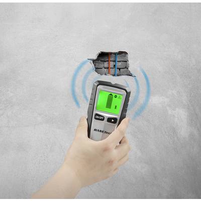 Eine Hand hält ein digitales Ortungsgerät an einer Wand mit einem Loch, dahinter sind rote und blaue Rohre. Das Gerät zeigt Ortungswellen.