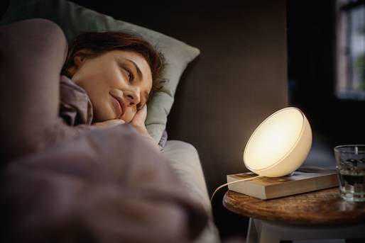 Eine Frau liegt im Bett und schaut in eine Nachtischlampe, die warmes Licht ausstrahlt.