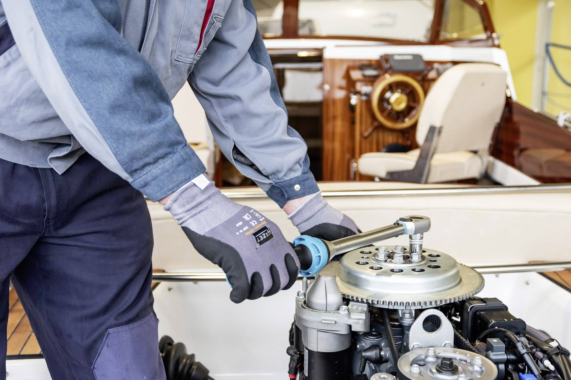 Person repariert Schiffsmaschine mit Drehmomentschlüssel auf einem Boot. Im Hintergrund ist das Armaturenbrett zu sehen.