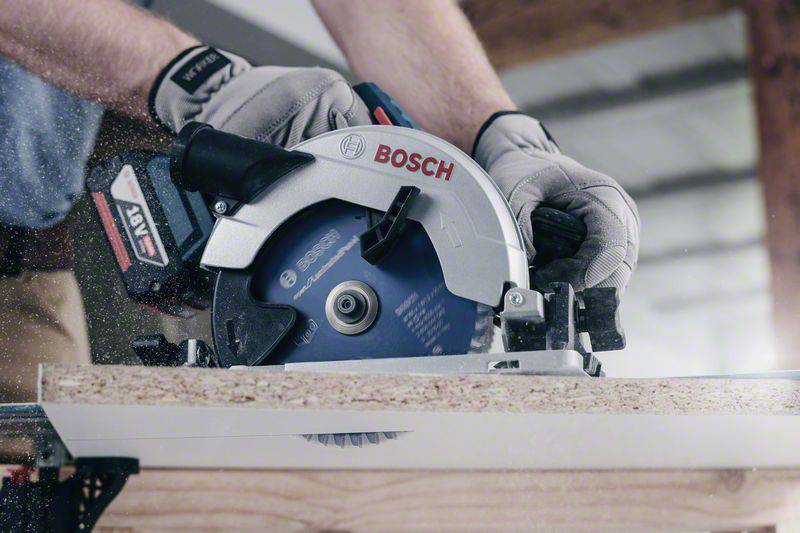 Eine Person schneidet mit einer Bosch Handkreissäge ein Stück Holz. Sägespäne sprühen in der Luft, Handschuhe schützen die Hände.