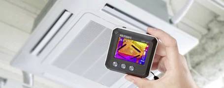 Eine Hand hält eine Wärmebildkamera, die Heizleistung einer Klimaanlage zeigt.