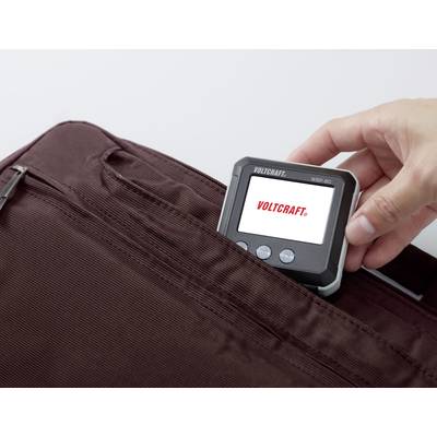 Hand steckt ein digitales Messgerät mit Bildschirm in eine braune Stofftasche. Auf dem Display steht 'VOLTCRAFT'.
