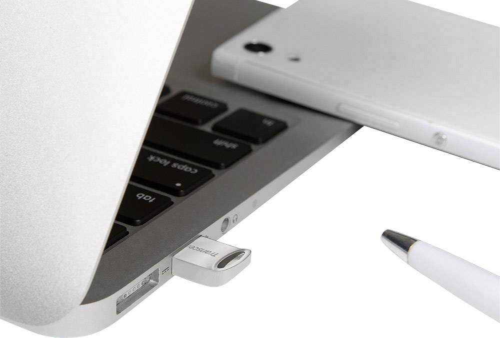 Nahaufnahme eines Laptops mit einem eingesteckten USB-Stick. Daneben ein Smartphone und ein Kugelschreiber. Technik im Einsatz.