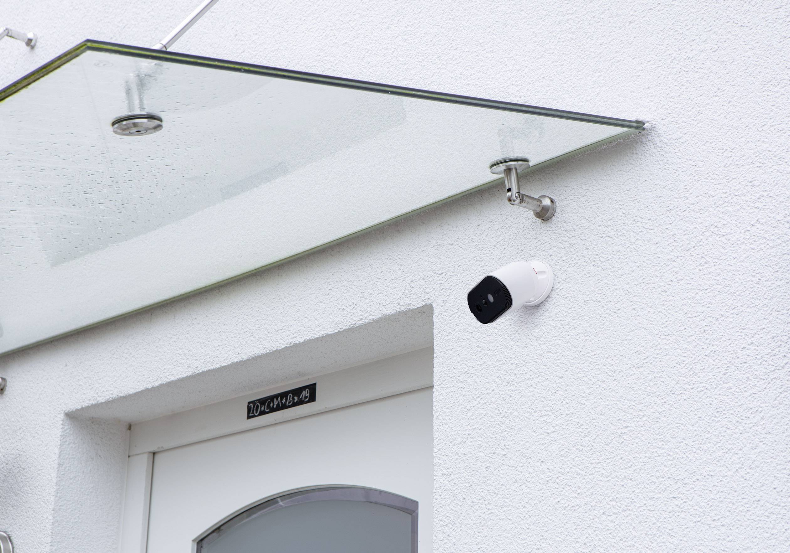 Haustür mit einem Sicherheitsglasvordach und einer Überwachungskamera an der Wand montiert.