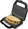 Sandwich mit Gemüse und Wurst in einem offenen Sandwichmaker. Brot ist goldbraun geröstet. Gerät auf schwarzer Oberfläche.
