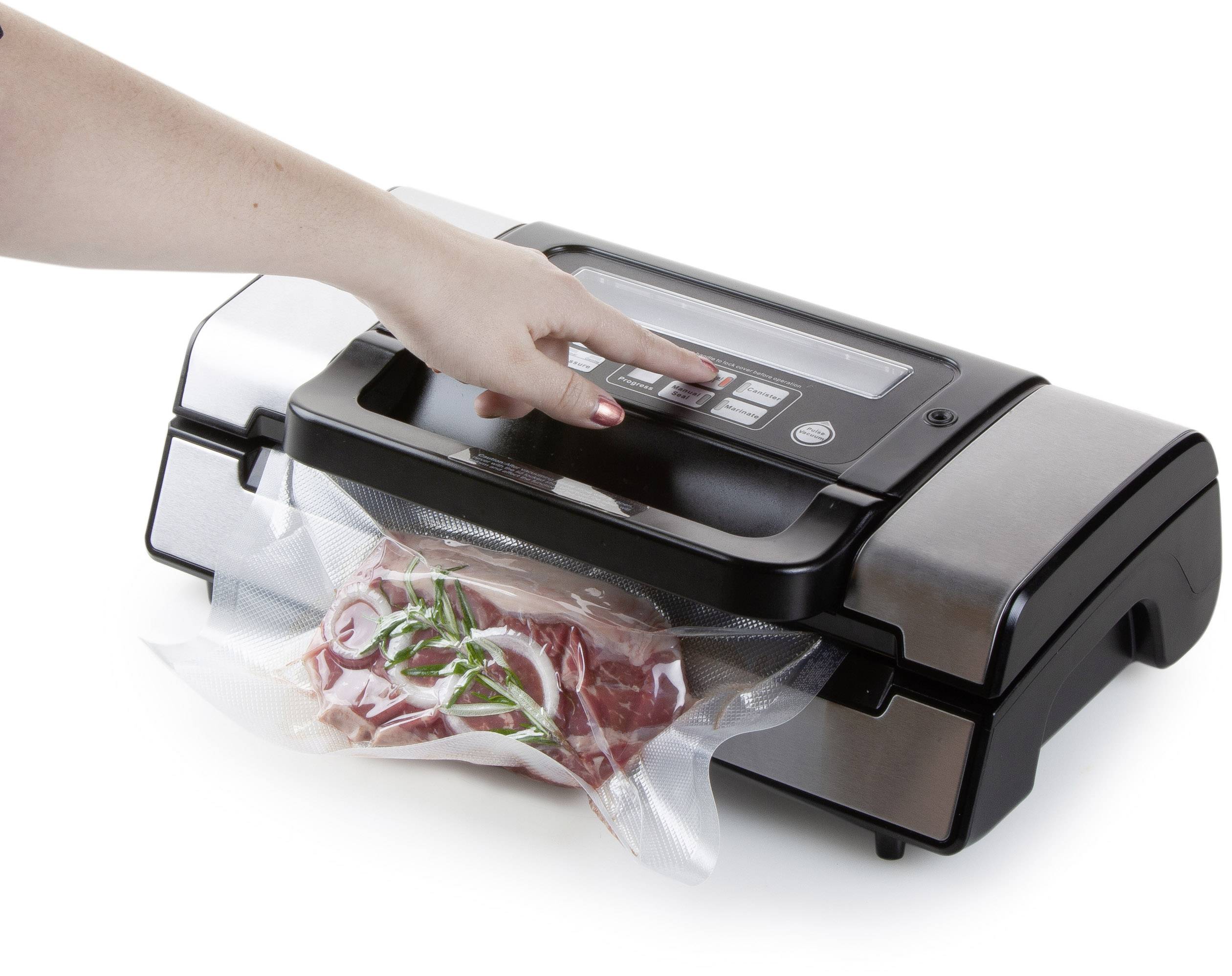 Eine Hand bedient ein Vakuumiergerät, das ein Stück rohes Fleisch mit Zwiebeln und Kräutern in einem Plastikbeutel verschließt.