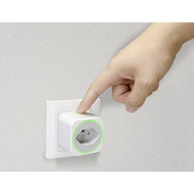 'Eine Hand steckt einen smarten Stecker in eine weiße Wandsteckdose, der Stecker leuchtet grün. Der Hintergrund ist beige.'
