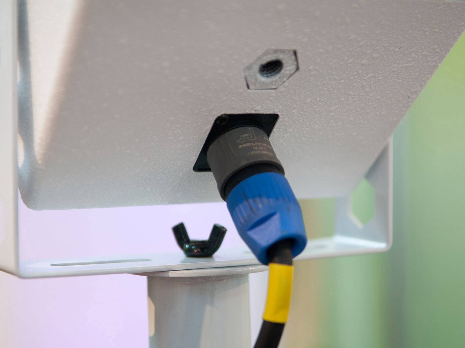 Ein blaues Kabel ist in ein elektronisches Gerät eingesteckt. Das Gerät scheint fest montiert zu sein. Im Hintergrund sind bunte Lichter verschwommen.