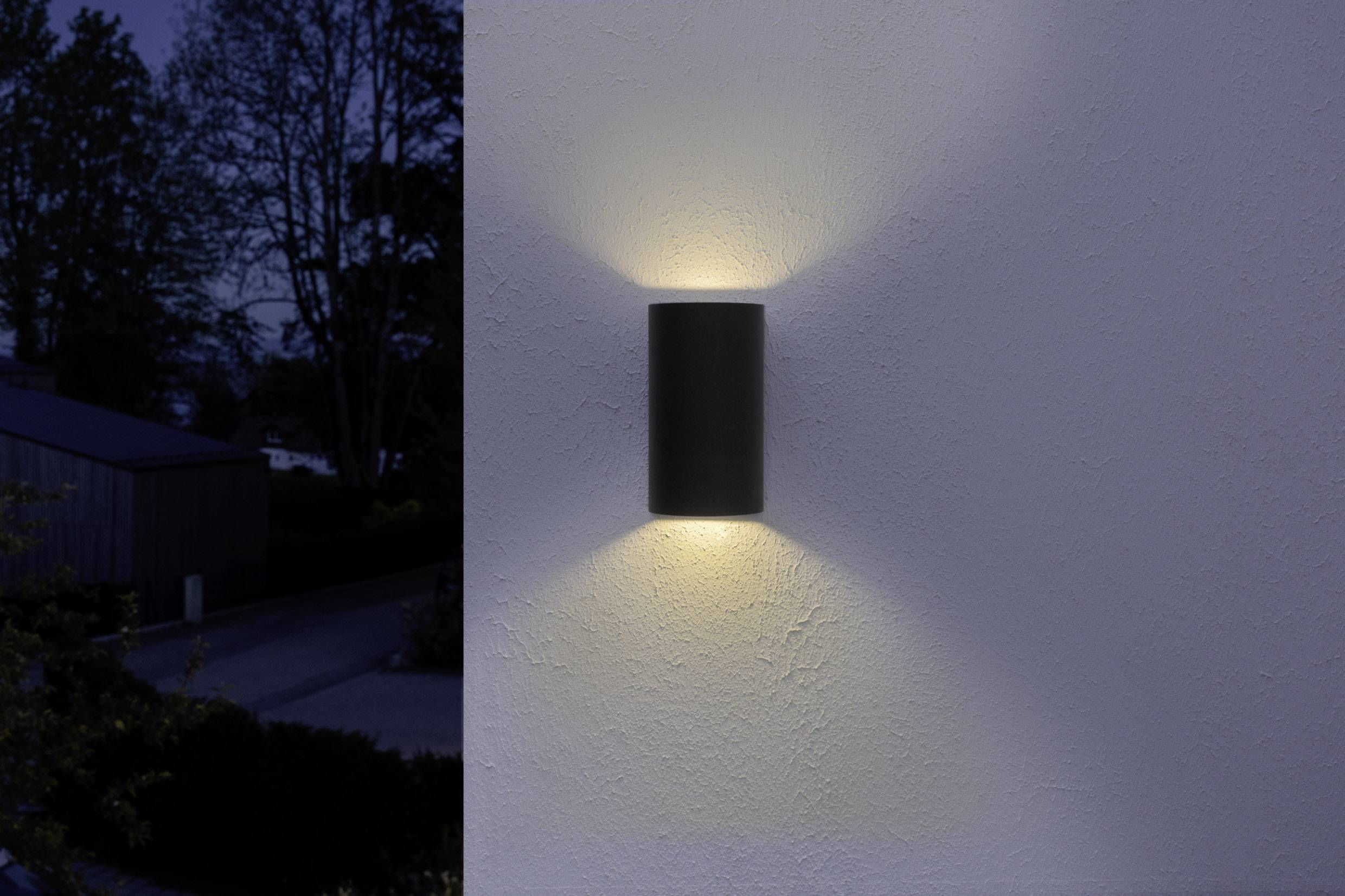Außenwandleuchte an einer Mauer, die ein warmes Licht nach oben und unten strahlt, beleuchtet eine dunkle, ruhige Straße.